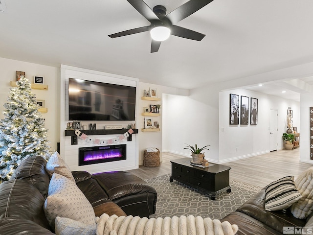 living room with ceiling fan, a large fireplace, and light wood-type flooring