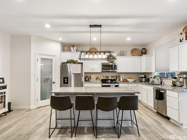 kitchen with a center island, white cabinets, hanging light fixtures, appliances with stainless steel finishes, and light hardwood / wood-style floors