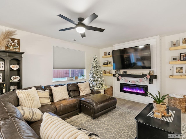 living room featuring wood-type flooring, a large fireplace, and ceiling fan