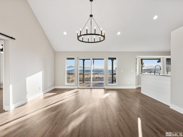 unfurnished living room featuring a mountain view, dark wood-type flooring, high vaulted ceiling, a barn door, and a chandelier