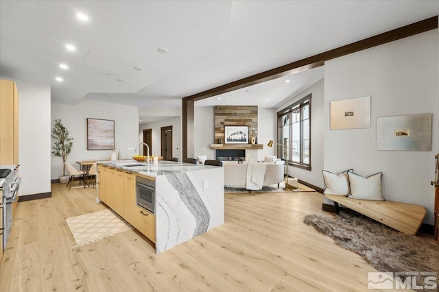 kitchen featuring light brown cabinets, a kitchen island with sink, sink, light hardwood / wood-style flooring, and light stone counters