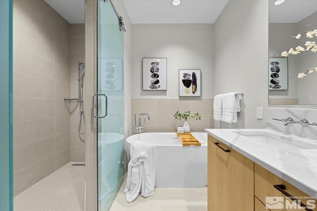 bathroom with separate shower and tub, vanity, and tile walls