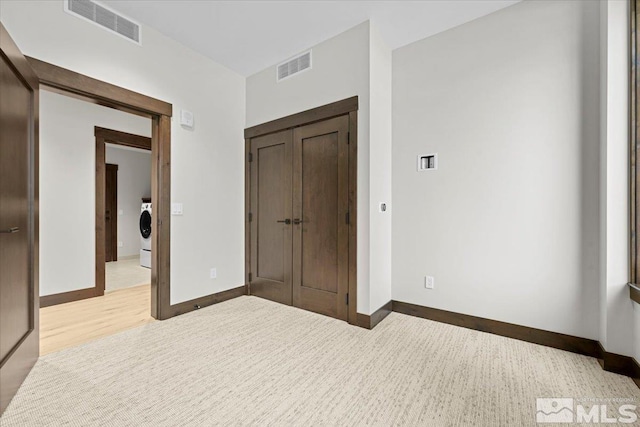 unfurnished bedroom with a closet, light hardwood / wood-style floors, and washer / dryer