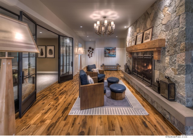 living room featuring french doors, hardwood / wood-style flooring, a stone fireplace, and a notable chandelier