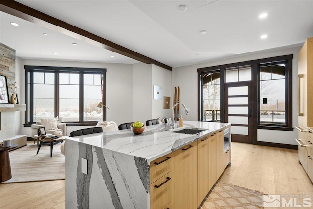 kitchen featuring a wealth of natural light, a large island, sink, and light stone counters