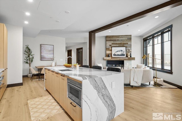 kitchen featuring light stone countertops, light brown cabinetry, a spacious island, and light hardwood / wood-style floors