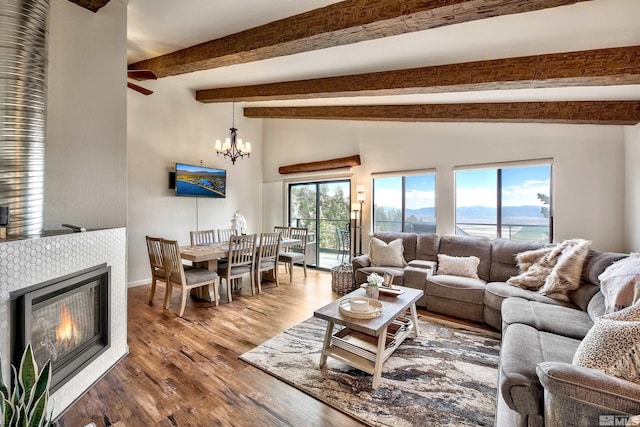 living room featuring a tile fireplace, lofted ceiling with beams, ceiling fan with notable chandelier, and hardwood / wood-style flooring