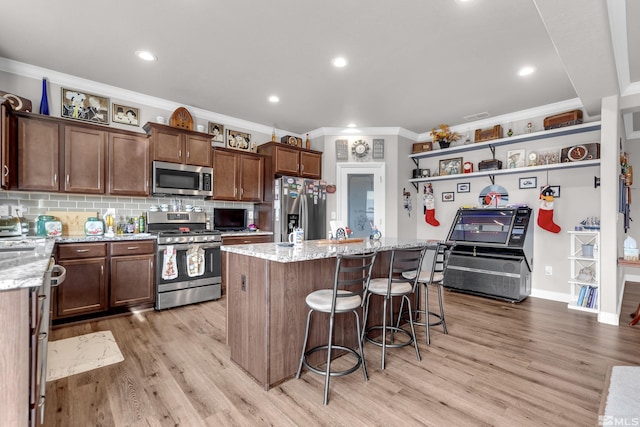 kitchen featuring appliances with stainless steel finishes, light stone counters, crown molding, light hardwood / wood-style flooring, and a center island