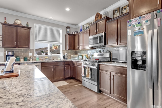 kitchen featuring light stone counters, backsplash, crown molding, light hardwood / wood-style floors, and appliances with stainless steel finishes