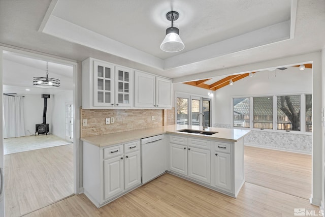 kitchen with dishwasher, a wood stove, sink, white cabinetry, and kitchen peninsula