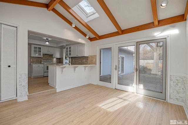 kitchen with a skylight, white electric range, beamed ceiling, kitchen peninsula, and light wood-type flooring