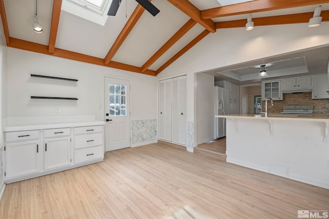 kitchen with a skylight, white appliances, light hardwood / wood-style floors, white cabinetry, and a breakfast bar area