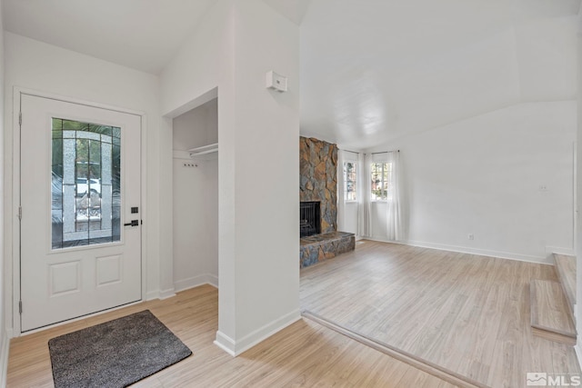 entrance foyer with vaulted ceiling, light hardwood / wood-style floors, a stone fireplace, and plenty of natural light