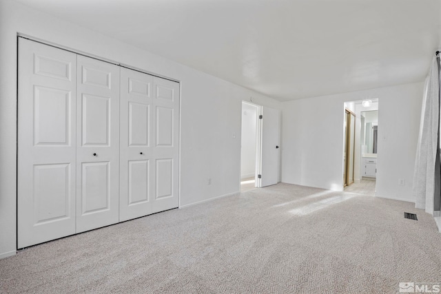 unfurnished bedroom featuring light carpet, ensuite bath, and a closet