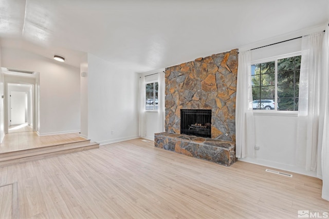 unfurnished living room with a stone fireplace, vaulted ceiling, and light wood-type flooring