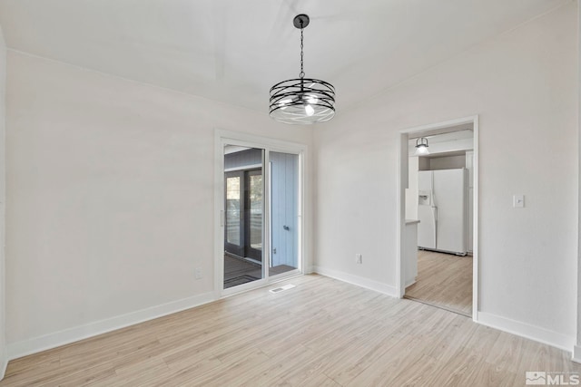 unfurnished room featuring a notable chandelier and light wood-type flooring