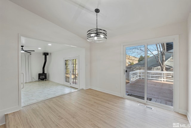 spare room featuring ceiling fan with notable chandelier, light wood-type flooring, a wood stove, and vaulted ceiling