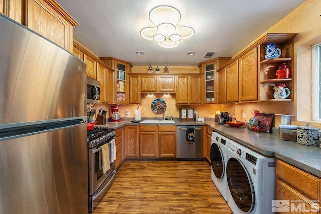 kitchen with washing machine and dryer, sink, stainless steel appliances, and light hardwood / wood-style floors