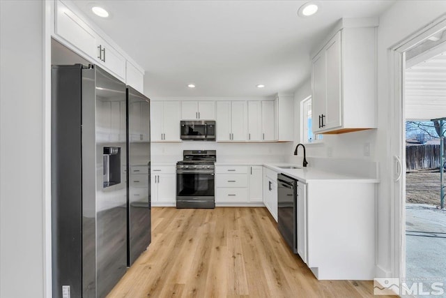 kitchen with sink, white cabinetry, appliances with stainless steel finishes, and light wood-type flooring