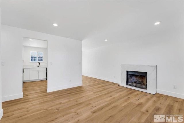 unfurnished living room featuring sink, light wood-type flooring, and a high end fireplace