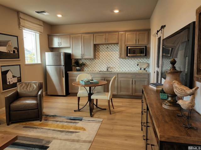 kitchen featuring backsplash, sink, light hardwood / wood-style flooring, a barn door, and appliances with stainless steel finishes