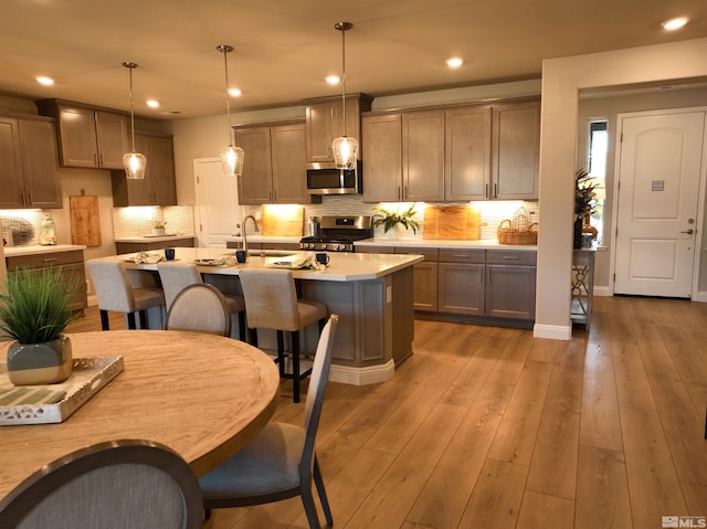 kitchen with a kitchen island with sink, stainless steel appliances, light hardwood / wood-style flooring, decorative light fixtures, and decorative backsplash