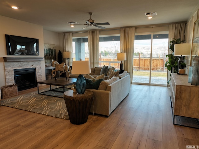 living room featuring ceiling fan, a stone fireplace, and light hardwood / wood-style flooring