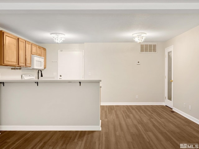 kitchen featuring hardwood / wood-style floors, a kitchen breakfast bar, sink, a notable chandelier, and kitchen peninsula