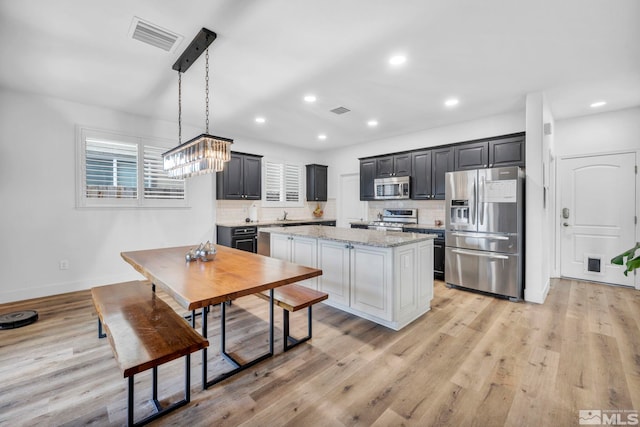 kitchen with pendant lighting, a center island, backsplash, appliances with stainless steel finishes, and light stone counters