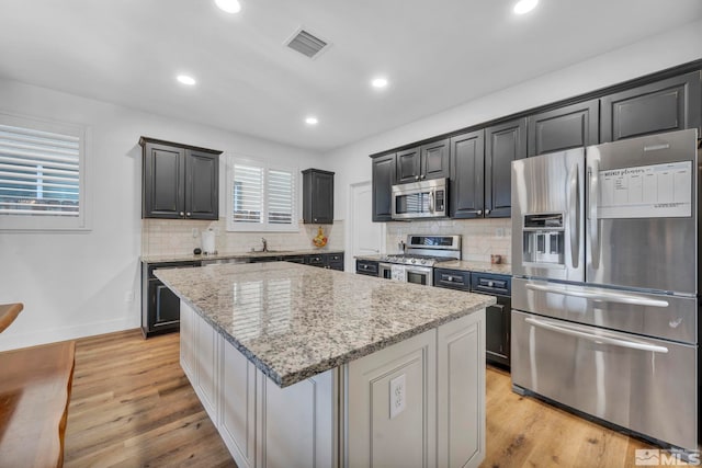 kitchen featuring light stone countertops, light wood-type flooring, stainless steel appliances, sink, and a center island