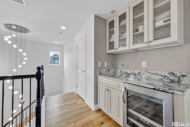 bar with light stone countertops, beverage cooler, sink, light hardwood / wood-style flooring, and white cabinets