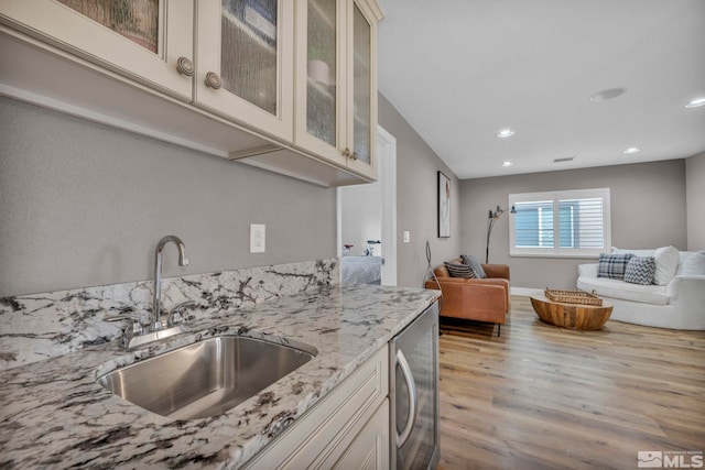 kitchen featuring light stone countertops, sink, beverage cooler, light hardwood / wood-style flooring, and cream cabinets