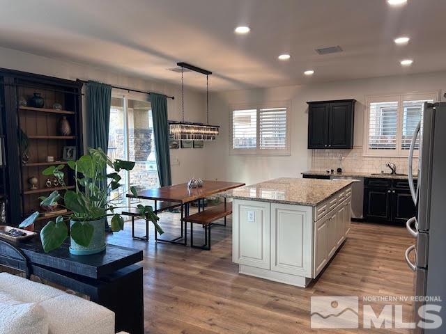 kitchen with white cabinets, hanging light fixtures, light wood-type flooring, appliances with stainless steel finishes, and a kitchen island