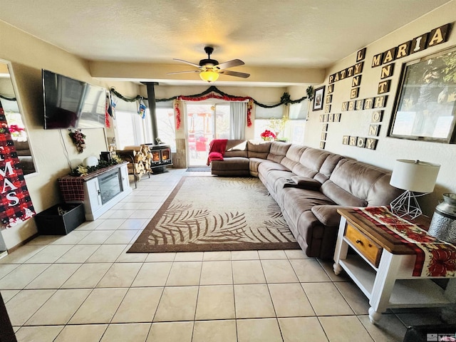 living room featuring a textured ceiling, a wood stove, ceiling fan, and light tile patterned flooring