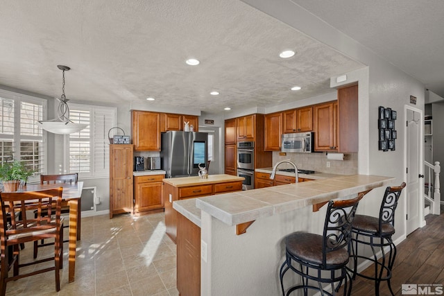 kitchen featuring hanging light fixtures, stainless steel appliances, tasteful backsplash, kitchen peninsula, and a breakfast bar