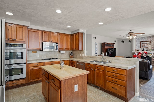 kitchen featuring a center island, sink, ceiling fan, kitchen peninsula, and stainless steel appliances