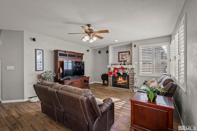 living room with a textured ceiling, a stone fireplace, ceiling fan, and dark hardwood / wood-style floors