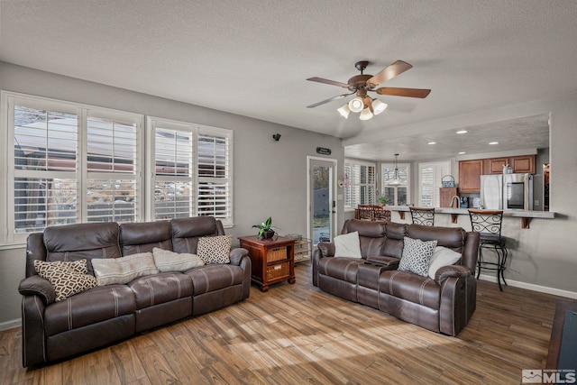 living room with ceiling fan, a textured ceiling, and light wood-type flooring