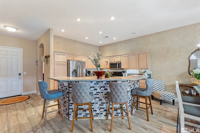 kitchen featuring light brown cabinetry, a breakfast bar, light hardwood / wood-style flooring, and appliances with stainless steel finishes