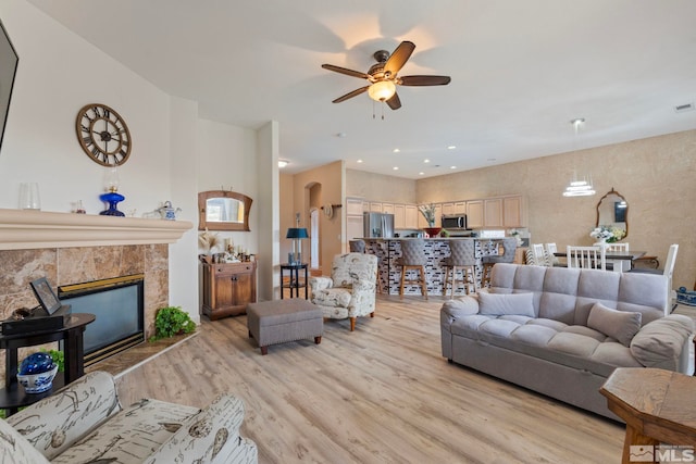 living room featuring light hardwood / wood-style floors, ceiling fan, and a tiled fireplace