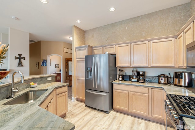 kitchen with light brown cabinets, sink, light wood-type flooring, light stone counters, and stainless steel appliances