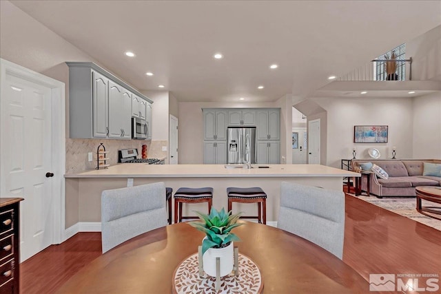 kitchen with decorative backsplash, kitchen peninsula, gray cabinetry, stainless steel appliances, and wood-type flooring