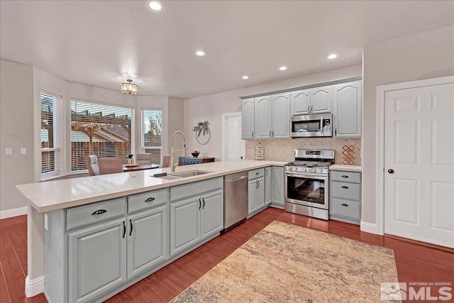 kitchen with decorative backsplash, appliances with stainless steel finishes, kitchen peninsula, sink, and wood-type flooring