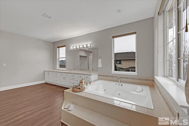 bathroom with vanity, a relaxing tiled tub, and wood-type flooring