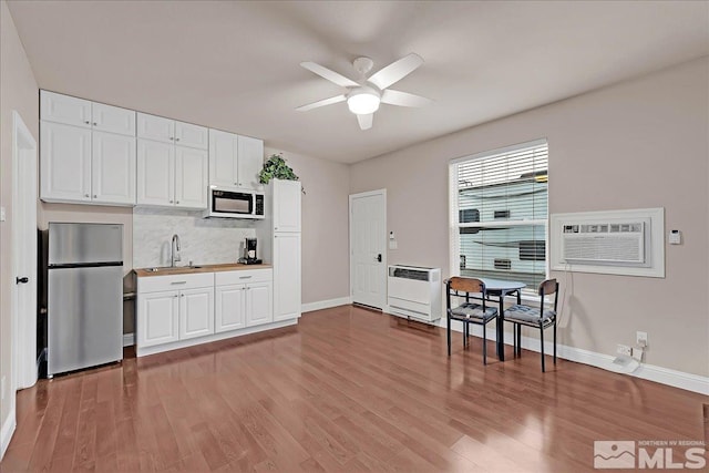 kitchen featuring stainless steel refrigerator, white cabinetry, sink, a wall unit AC, and heating unit