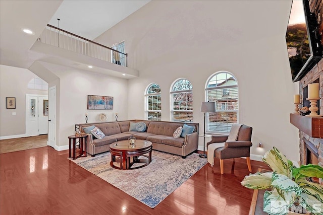 living room featuring a high ceiling, hardwood / wood-style flooring, and a stone fireplace