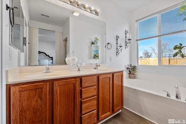 bathroom with hardwood / wood-style flooring, vanity, and tiled bath