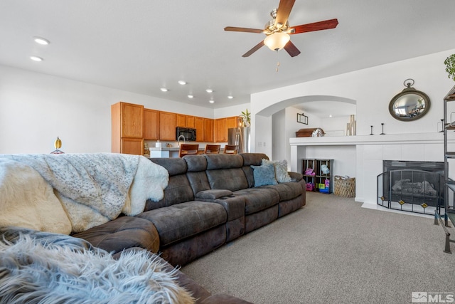 living room featuring ceiling fan, a tiled fireplace, and carpet