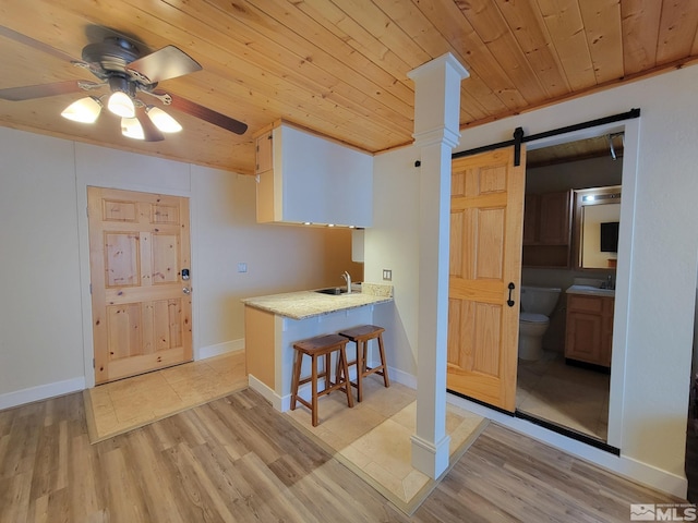 kitchen featuring a kitchen bar, kitchen peninsula, sink, a barn door, and wooden ceiling