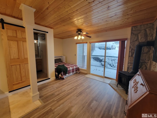 bedroom featuring wooden ceiling, a wood stove, ensuite bathroom, light hardwood / wood-style flooring, and ceiling fan